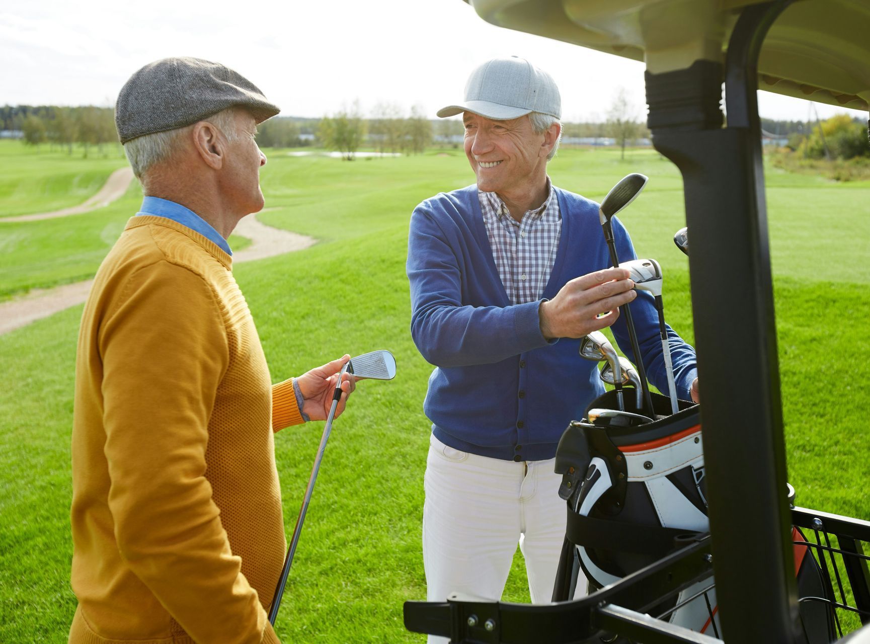 Two men are standing next to a golf cart on a golf course.
