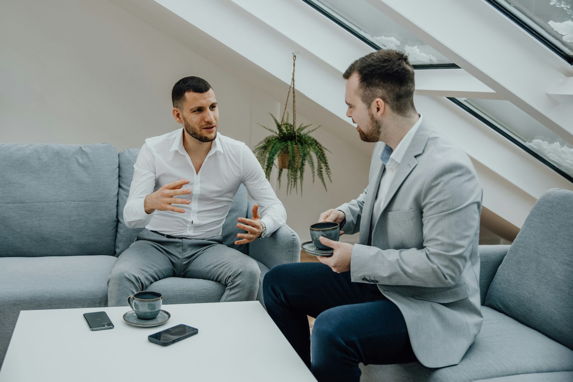 Two men are sitting on a couch talking to each other.