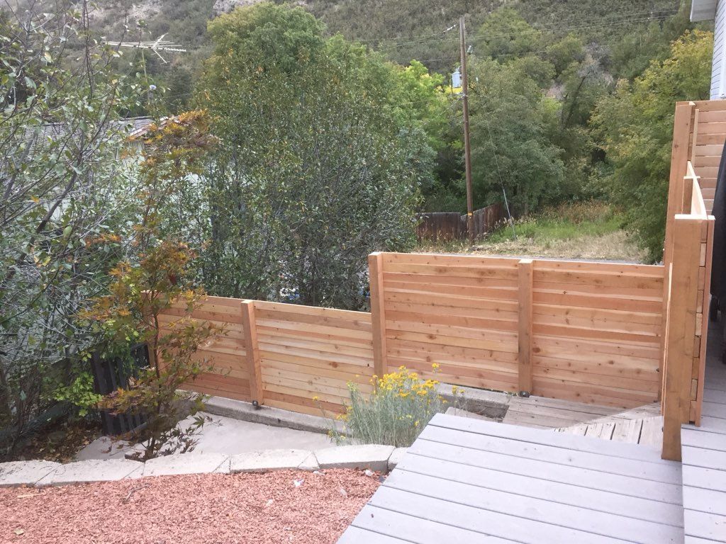 Wooden backyard fence and deck beside a garden path with trees and shrubs