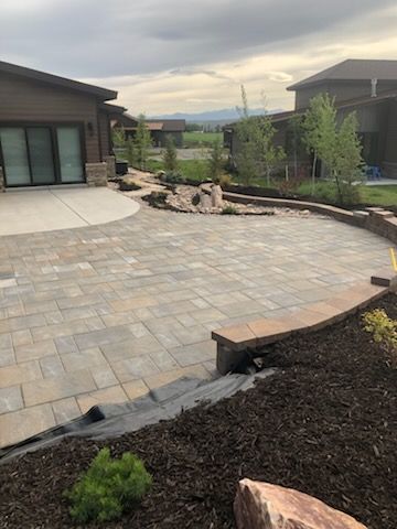 Backyard stone patio with curved retaining wall, mulch beds, and modern house exteriors