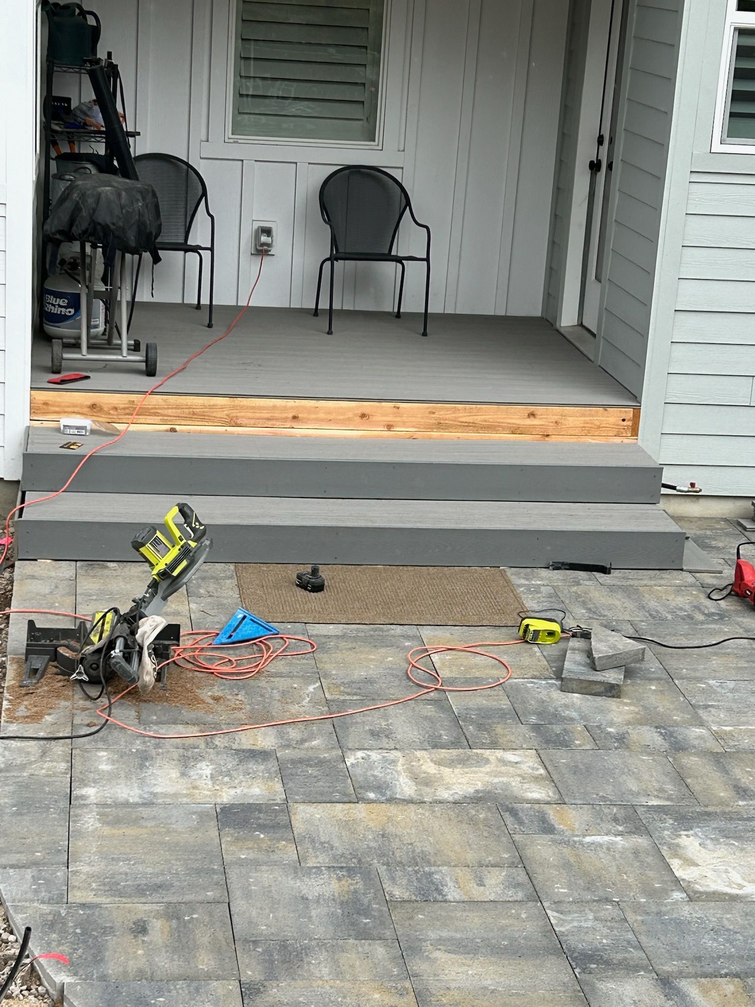 Front porch with two chairs and potted plants, showing a damaged step and debris on the pavers.
