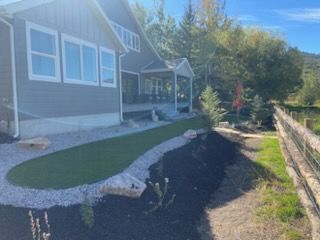 House with a sloped yard and retaining wall beside a dirt path in sunny outdoor setting