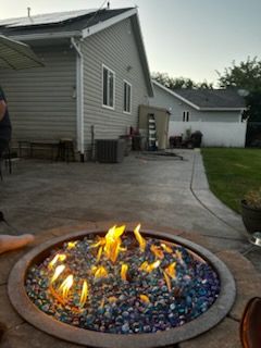 Backyard fire pit with colorful glass stones and flames beside a patio and house