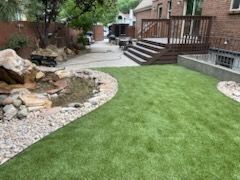 Backyard with green lawn, stone-edged pond, and wooden deck beside a brick house