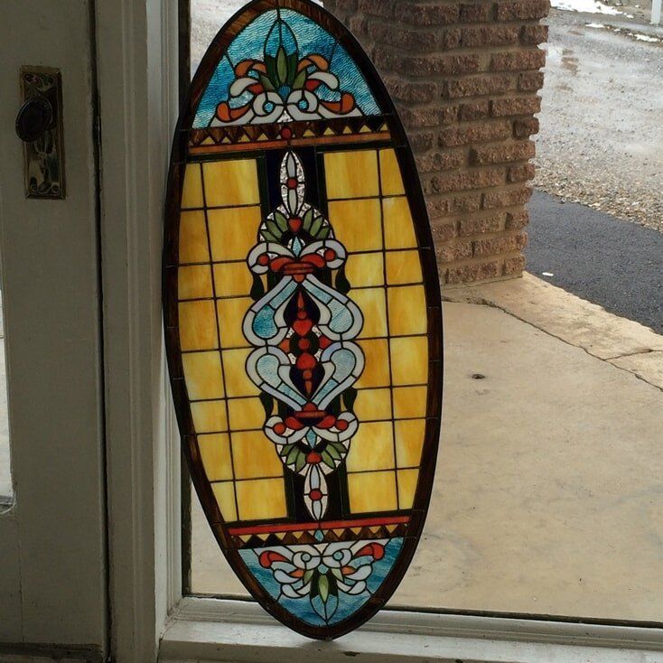 Oval stained glass window with a central ornate design, set in a window frame.