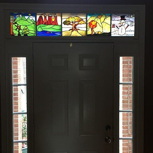 Stained glass panels above a door depict seasons: a tree, mountains, and a snowman.