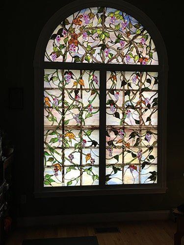 Stained glass window depicting a tree with colorful leaves and purple flowers.