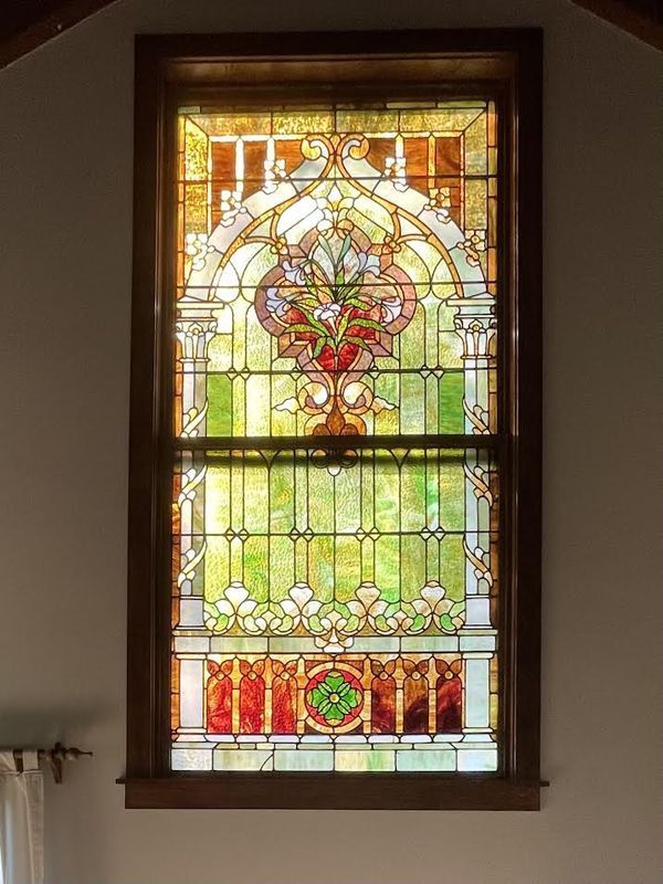 Stained glass window with floral design, set in a wooden frame. Green, red, and yellow colors are prominent.