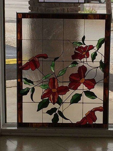 Stained-glass panel with red flowers and green leaves on a clear, grid-patterned background, brown border.