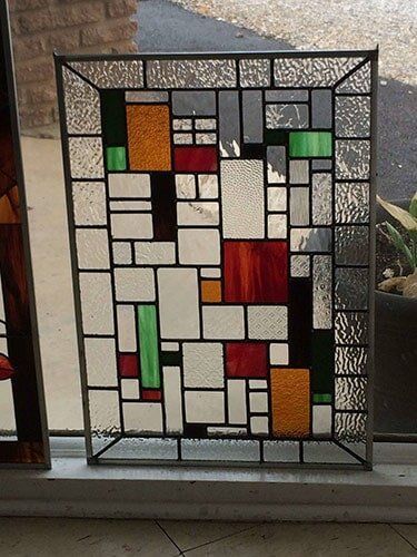Stained glass panel with geometric design; rectangles of clear, red, orange, and green glass within a black border.