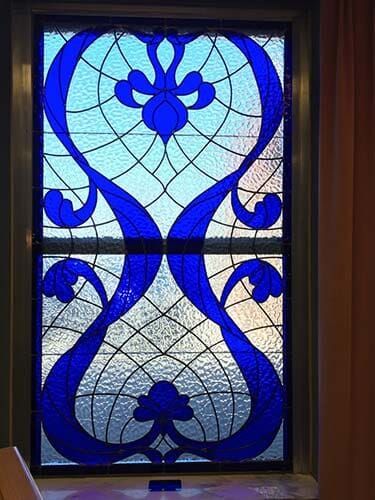 Stained glass window with blue floral design and intricate web-like background.