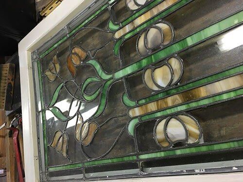 Stained glass window with tan, green, and clear glass floral design in a white frame.