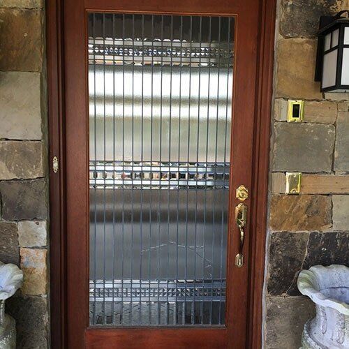 Wooden door with vertical metal bars and glass, set in stone wall.