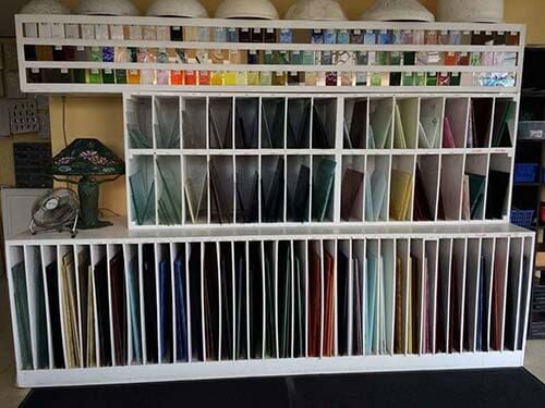 A wall-mounted display of glass sheets in various colors and shades, in a studio setting.