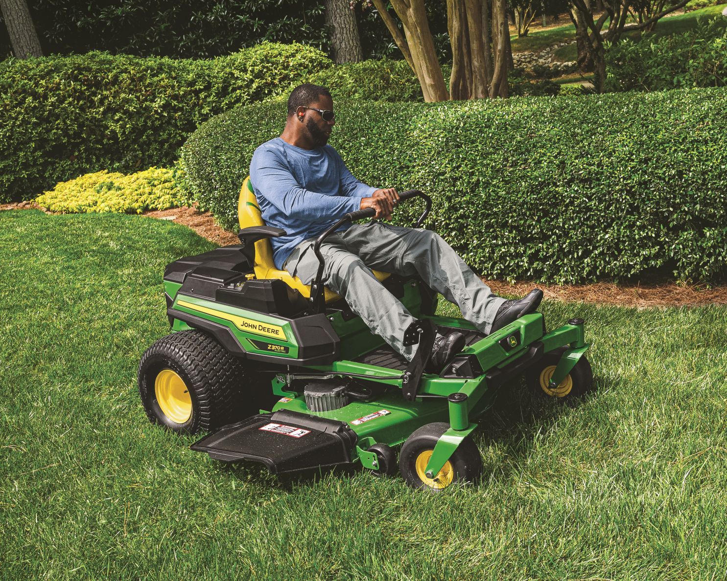 A green and yellow John Deere riding lawn mower sits in a residential yard on a sunny day. A green and yellow John Deere riding lawn mower sits in a residential yard on a sunny day.