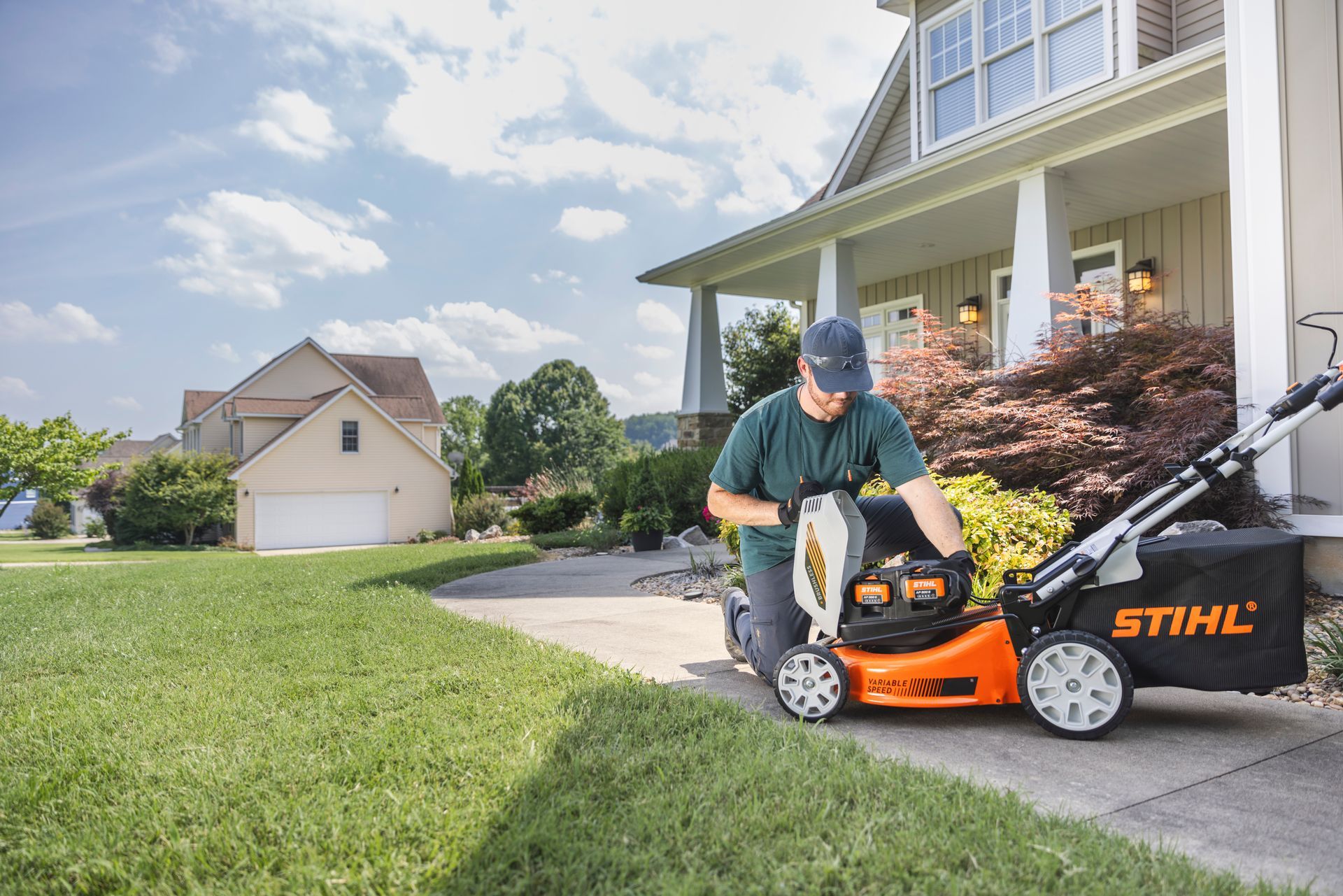 Two orange and gray power gardening tools with long handles stand on a grassy lawn in front of a hedge.