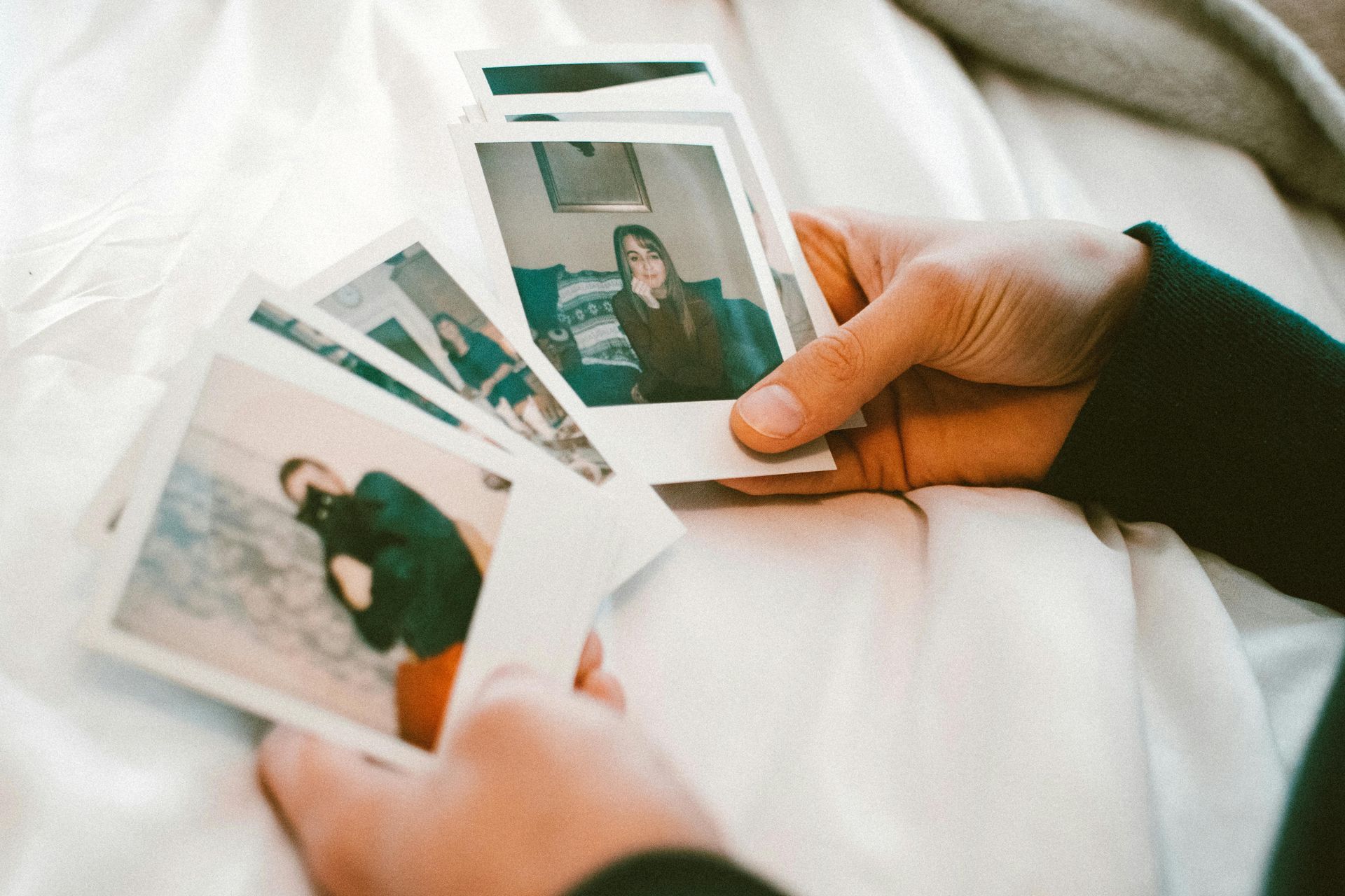 Mains tenant et regardant une pile de photos Polaroid sur une surface blanche.