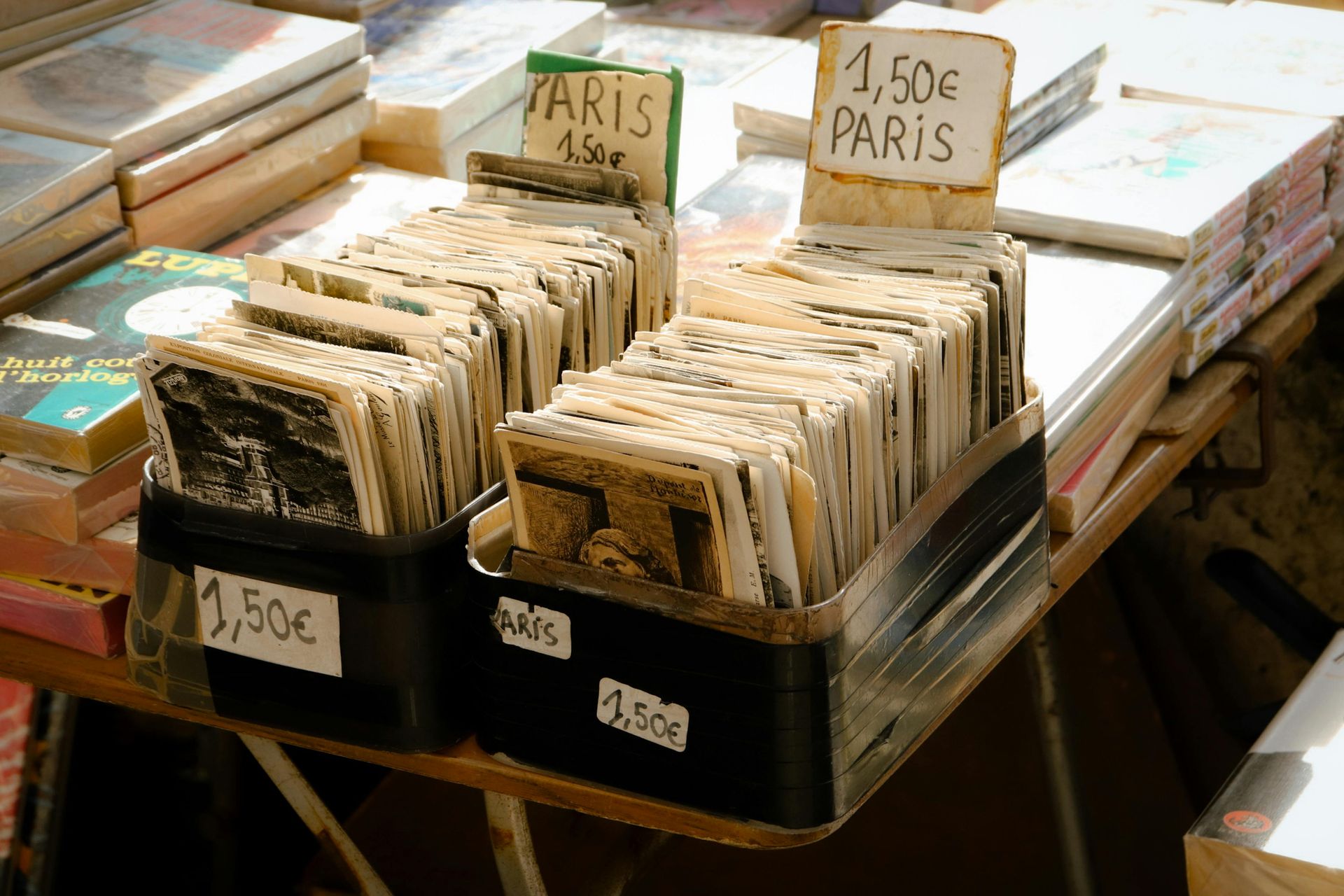 Livres en vente sur un marché parisien ; beaucoup en petites piles, avec des panneaux de prix.