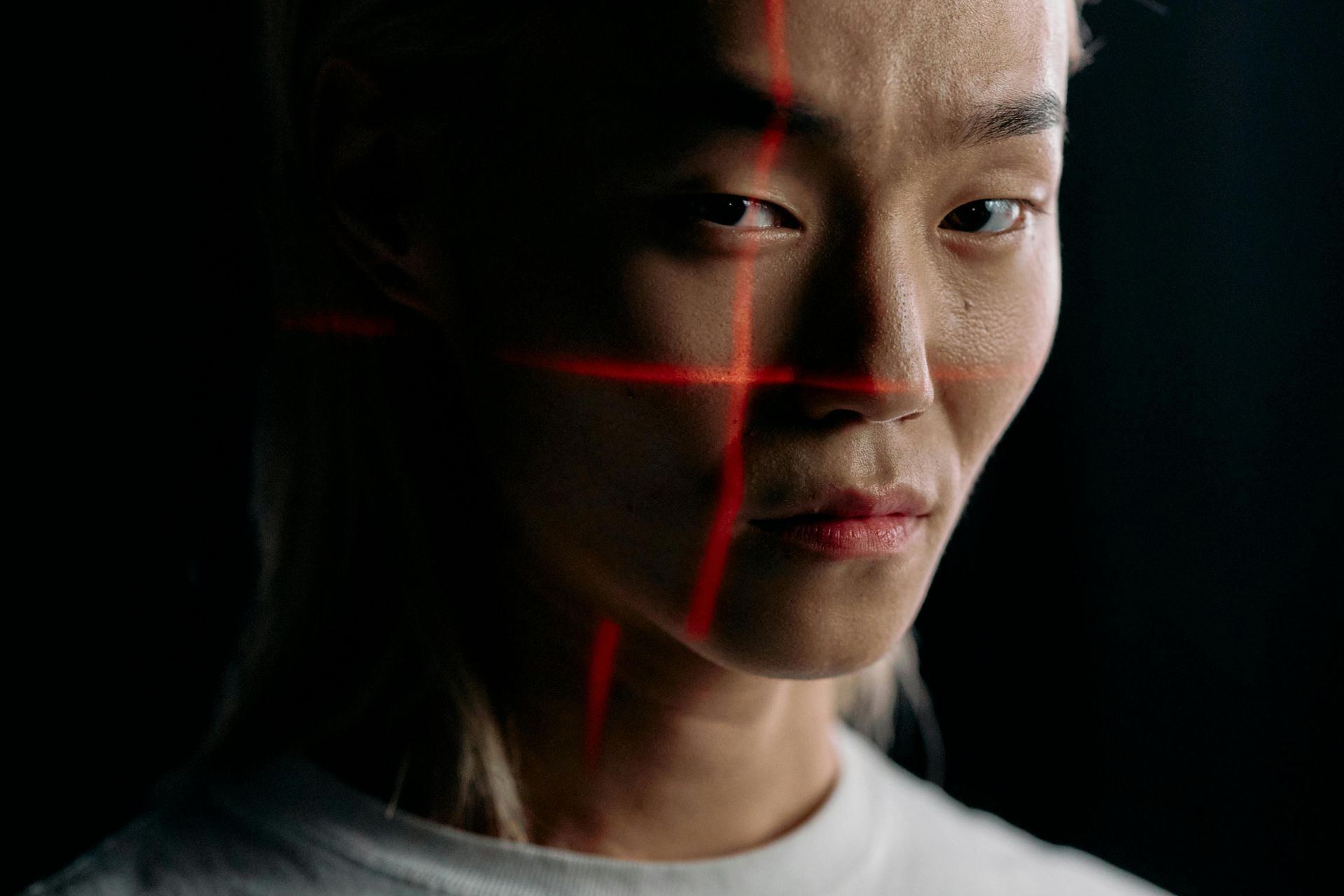Personne asiatique avec une grille laser rouge projetée sur le visage, fond sombre.