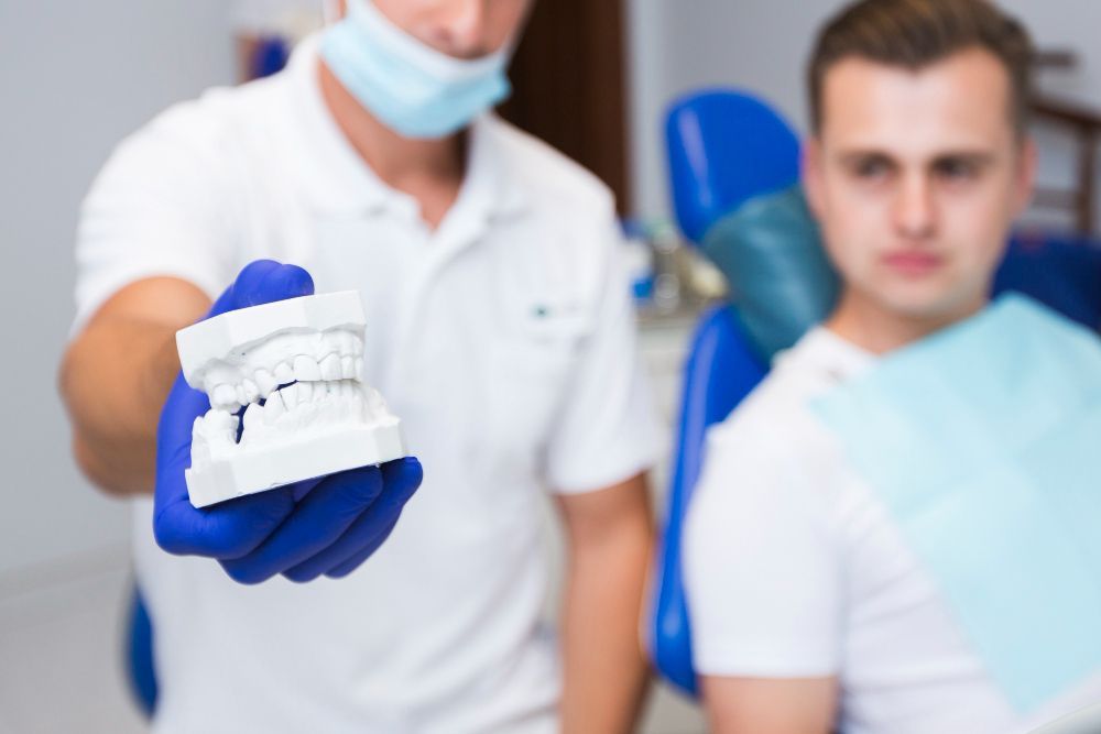 Dentist holding a white teeth model, explaining to a patient in a dental chair.