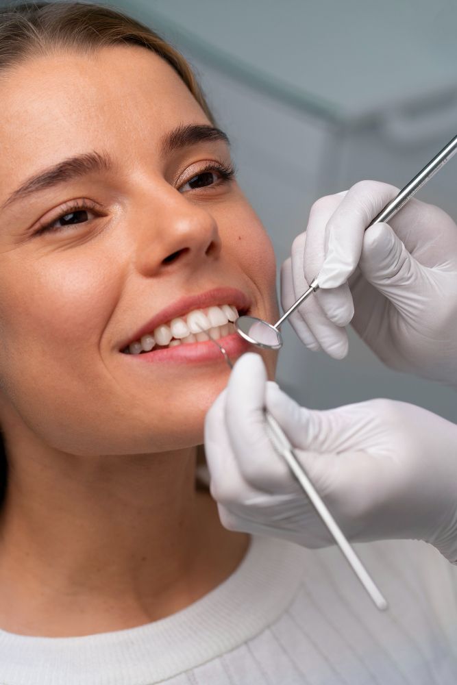 Woman at dentist smiling, being examined with dental tools. White gloves, dental office setting.