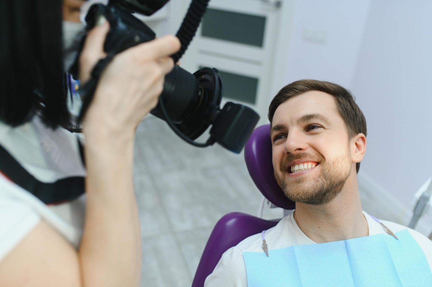 Dentist taking a photo of a smiling man in a dental chair.