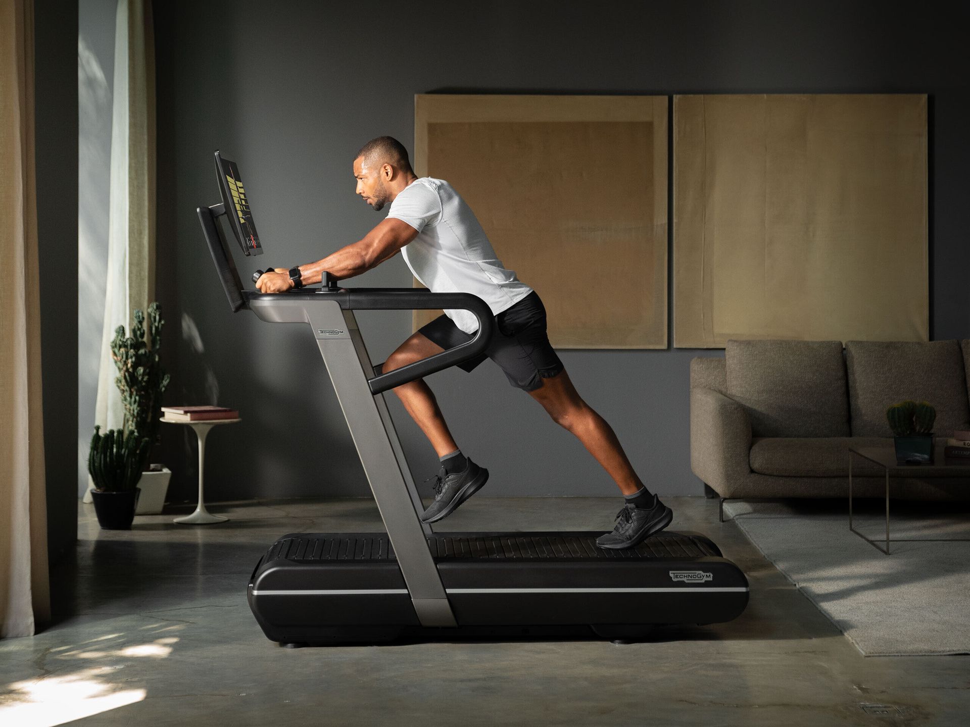 A person in athletic gear uses a sleek black treadmill in a modern, dimly lit home living room.