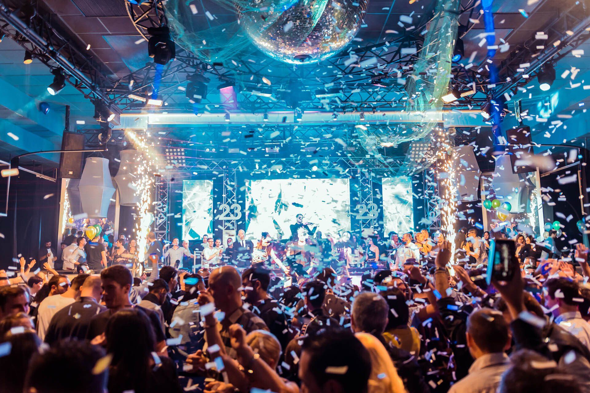 A crowd of people are dancing in a club with confetti falling from the ceiling.