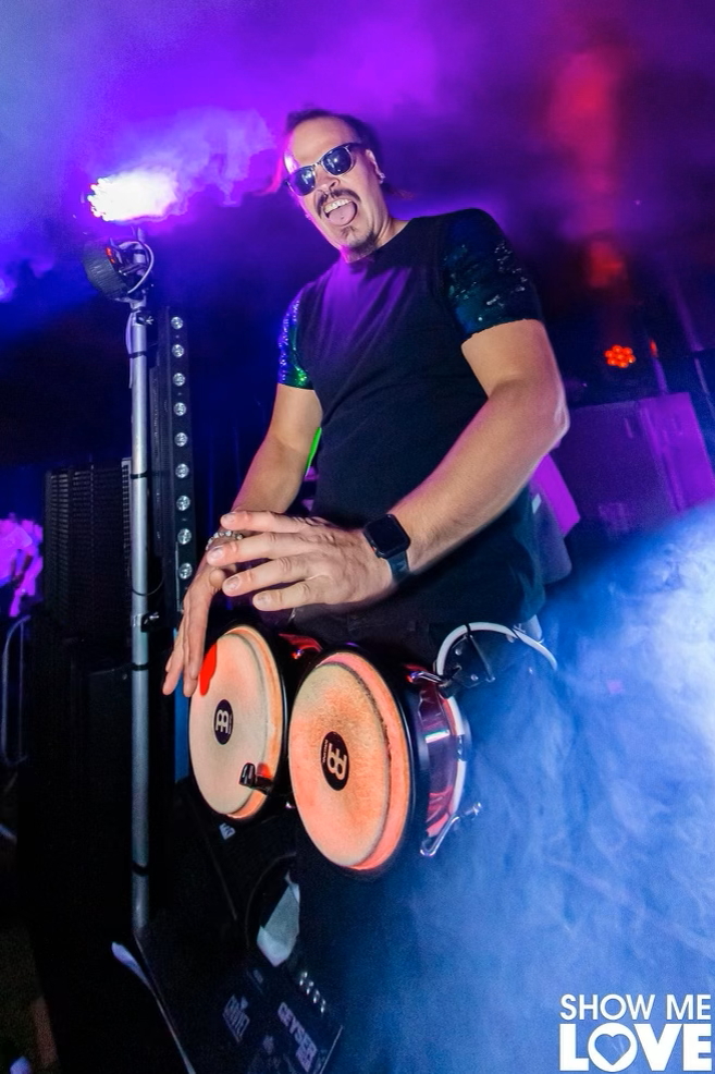 A man is playing drums on a stage in a dark room.