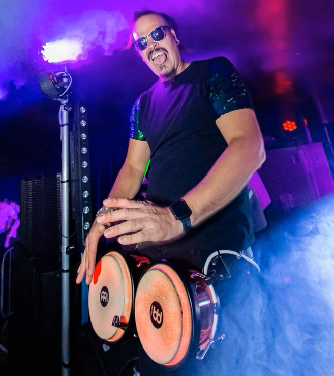 A man is sitting on a drum set in a dark room.