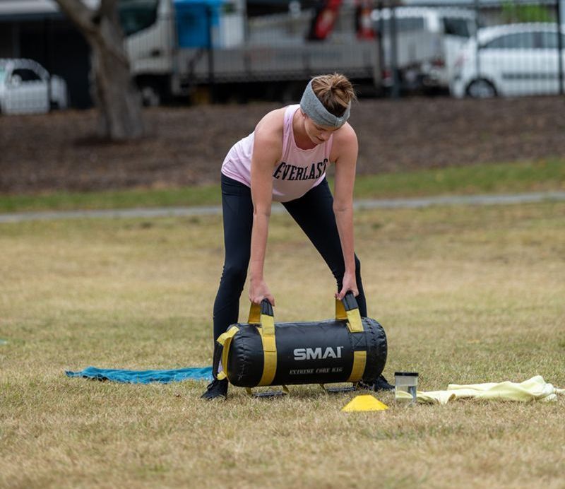 A woman is lifting a small bag in a field.