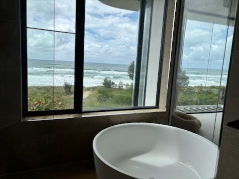 A Modern Bathroom with A White Tub and A Large Window Overlooking the Ocean — KirraLina Cleaning Services in Tweed Heads, NSW