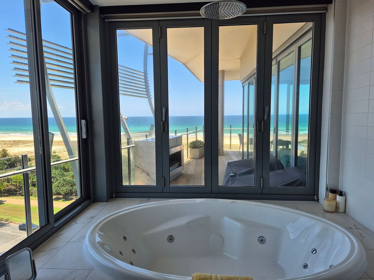 A White Oval Jacuzzi in A Bathroom with Large Glass Doors — KirraLina Cleaning Services in Tweed Heads, NSW
