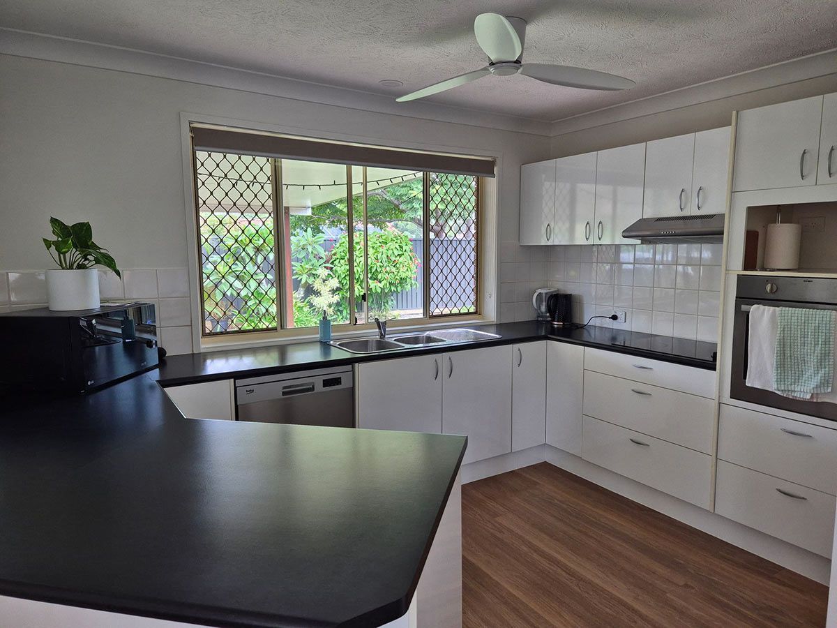 A Bright Kitchen with White Cabinets, a Black Countertop — KirraLina Cleaning Services in Tweed Heads, NSW