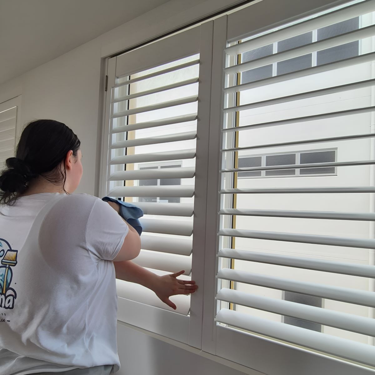 A Woman Is Cleaning a Window with Shutters — KirraLina Cleaning Services in Tweed Heads, NSW