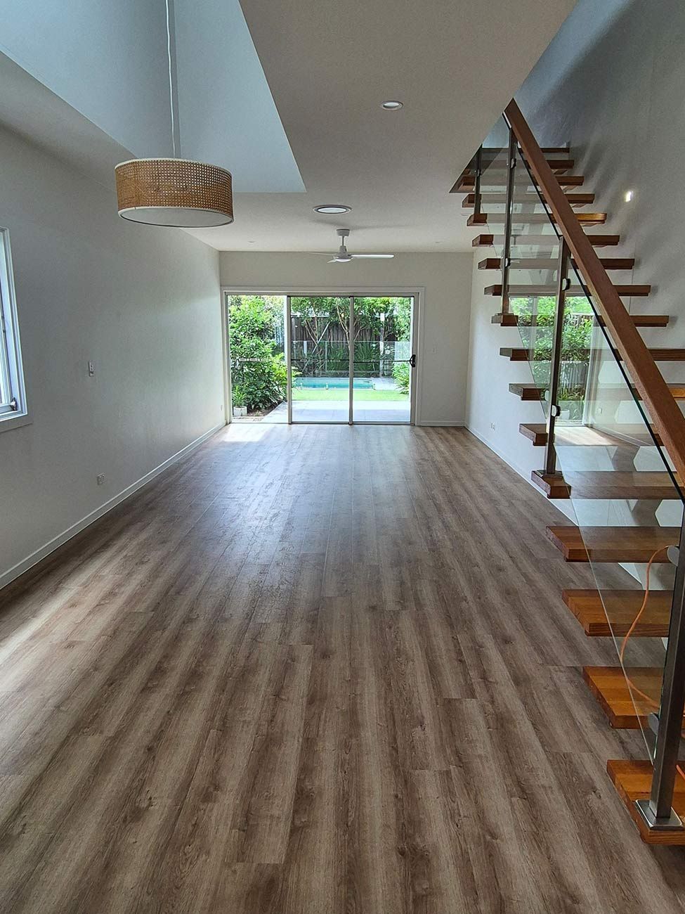 Empty Living Room with Wooden Flooring, a Staircase, and Sliding Glass Doors Leading to A Backyard — KirraLina Cleaning Services in Tweed Heads, NSW