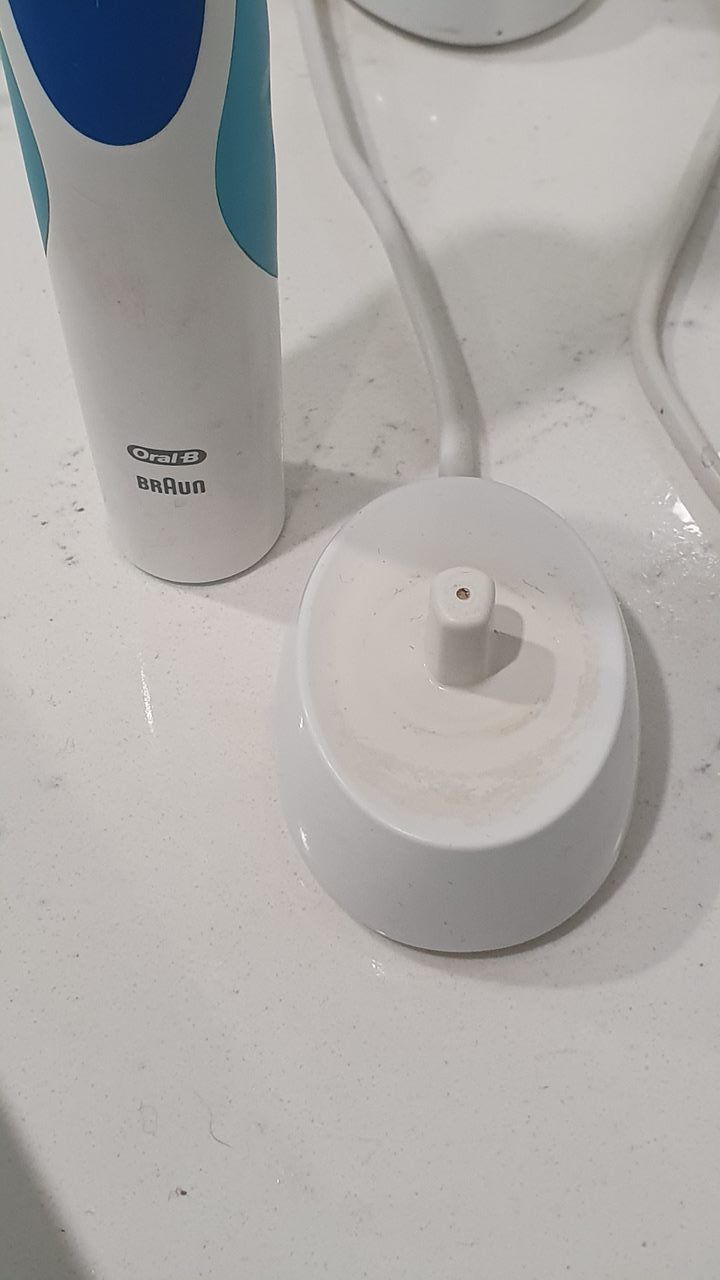 An Electric Toothbrush is Sitting on a White Counter Next to a Charging Base — KirraLina Cleaning Services in Tweed Heads, NSW