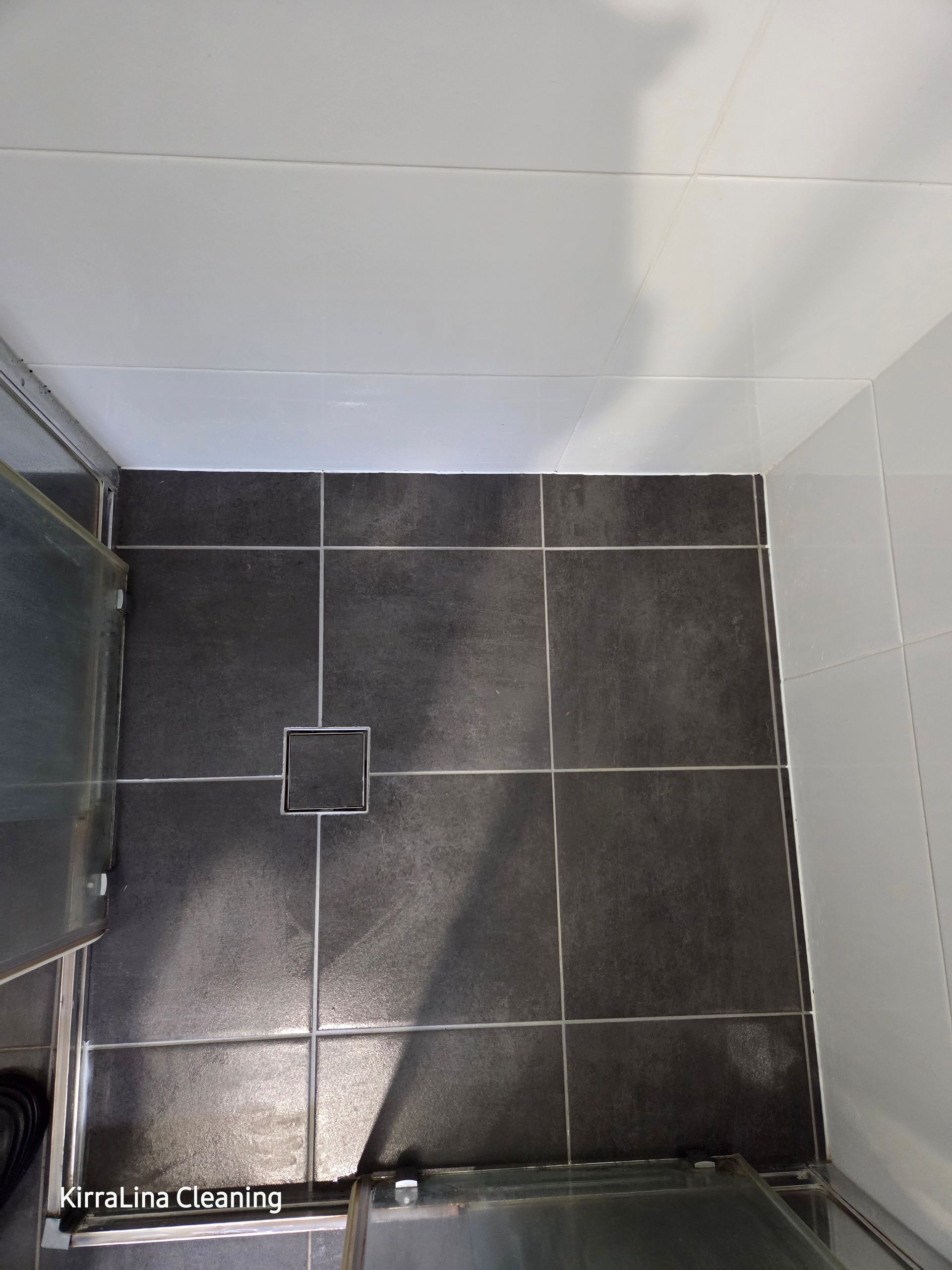 Top-down view of a small tiled shower floor with a central drain and white walls. — KirraLina Cleaning Services in Tweed Heads, NSW