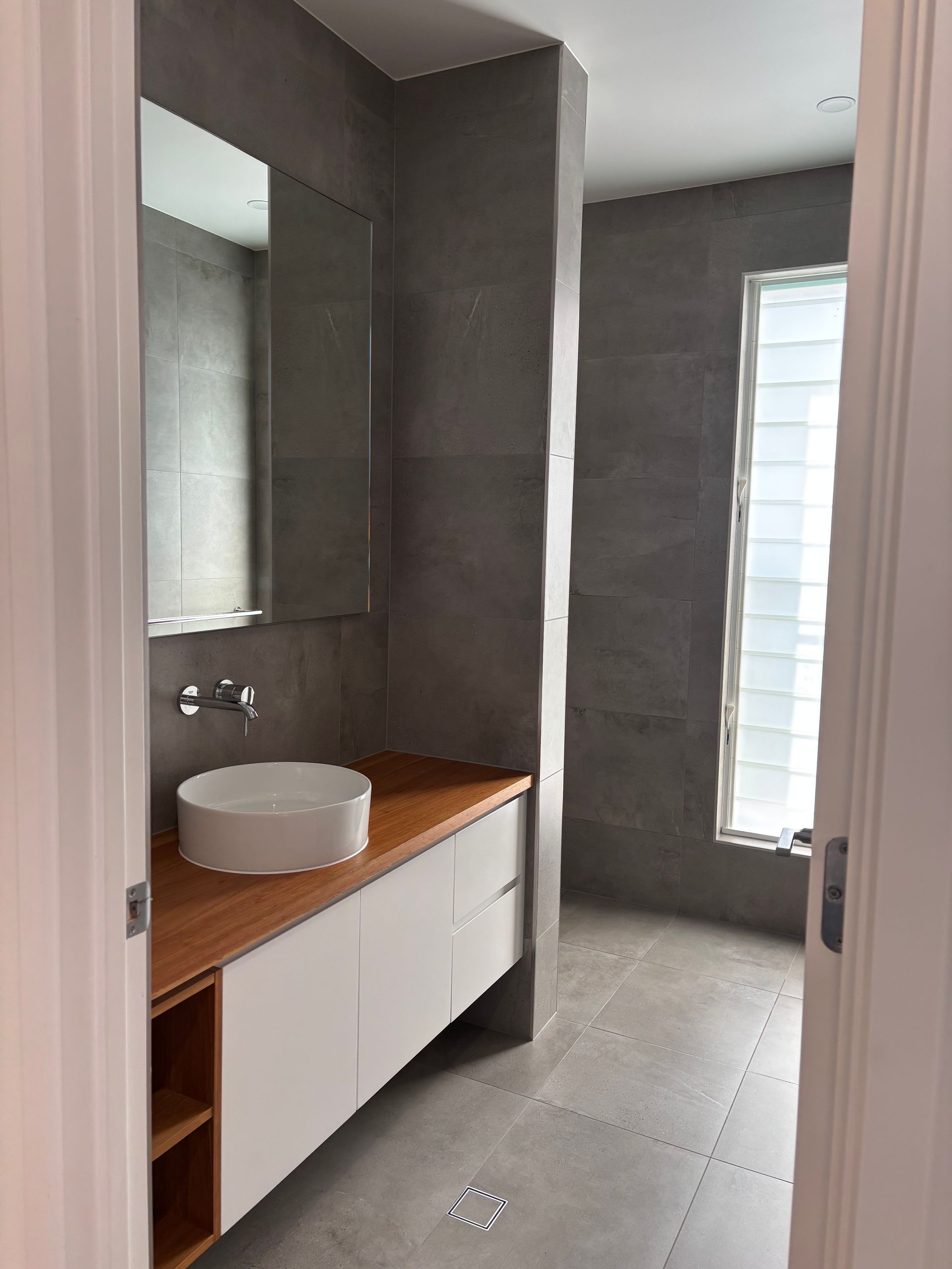 Modern bathroom with gray tiles, white sink, wooden vanity, and window — KirraLina Cleaning Services in Tweed Heads, NSW