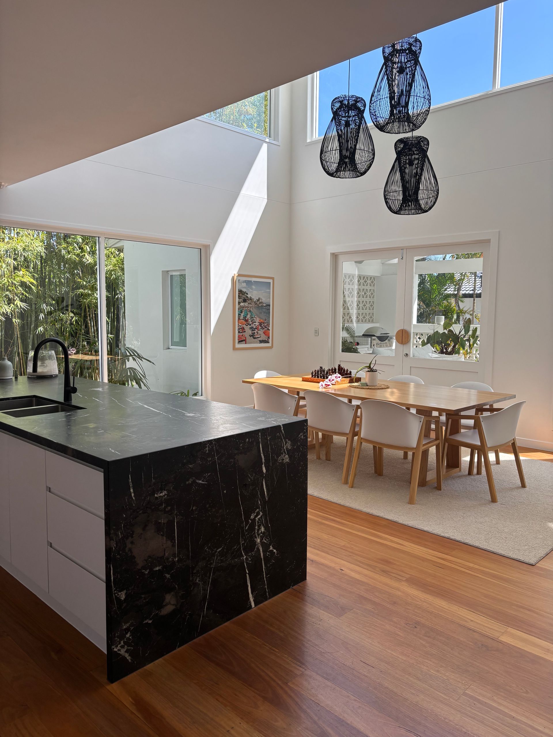 Modern kitchen with black island, dining table, and skylight. Wooden floors, white walls, and decorative pendant lights — KirraLina Cleaning Services in Tweed Heads, NSW