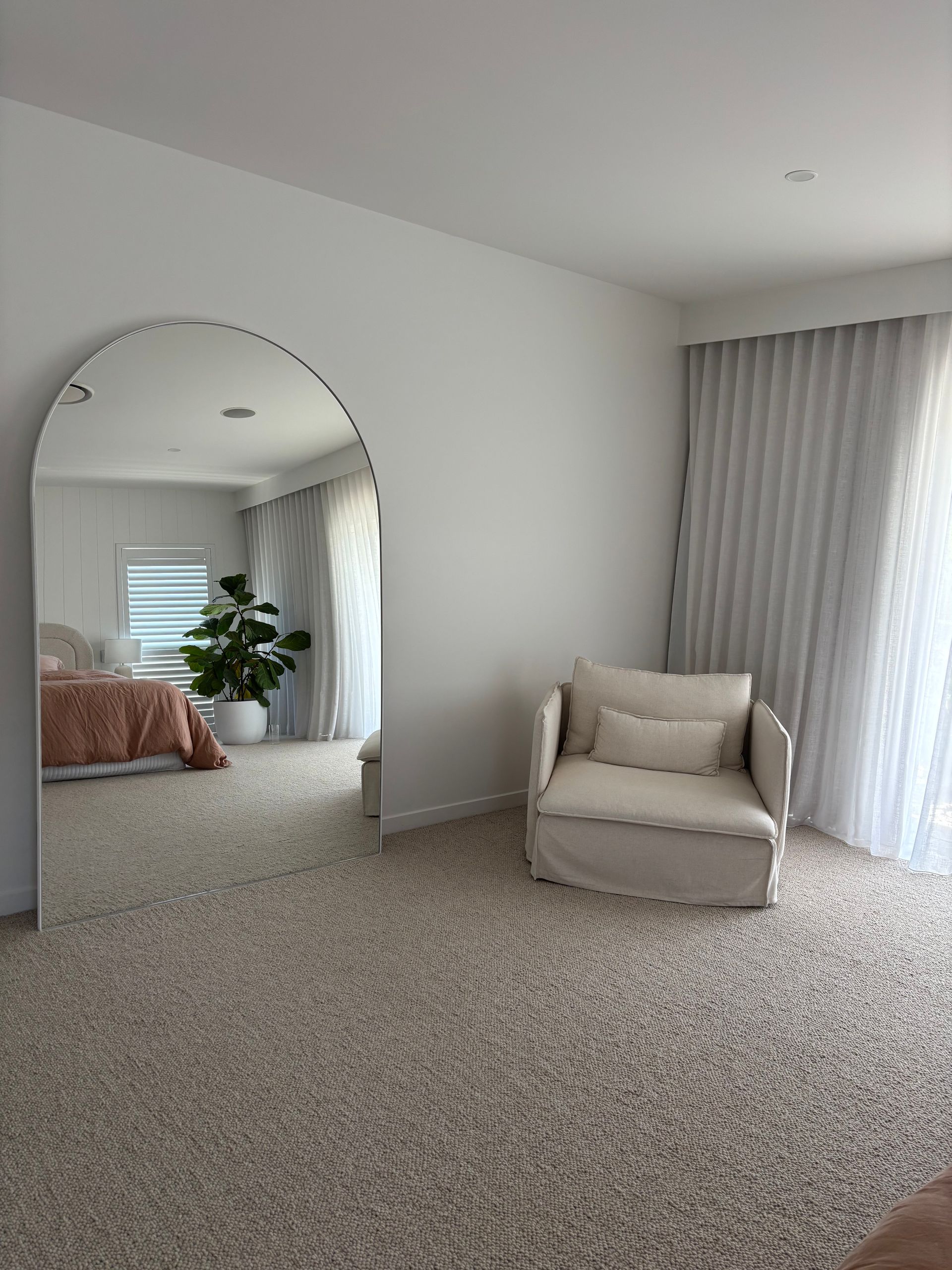 Large arched mirror reflecting a bedroom with a bed, armchair, and curtains. Beige and white color palette — KirraLina Cleaning Services in Tweed Heads, NSW