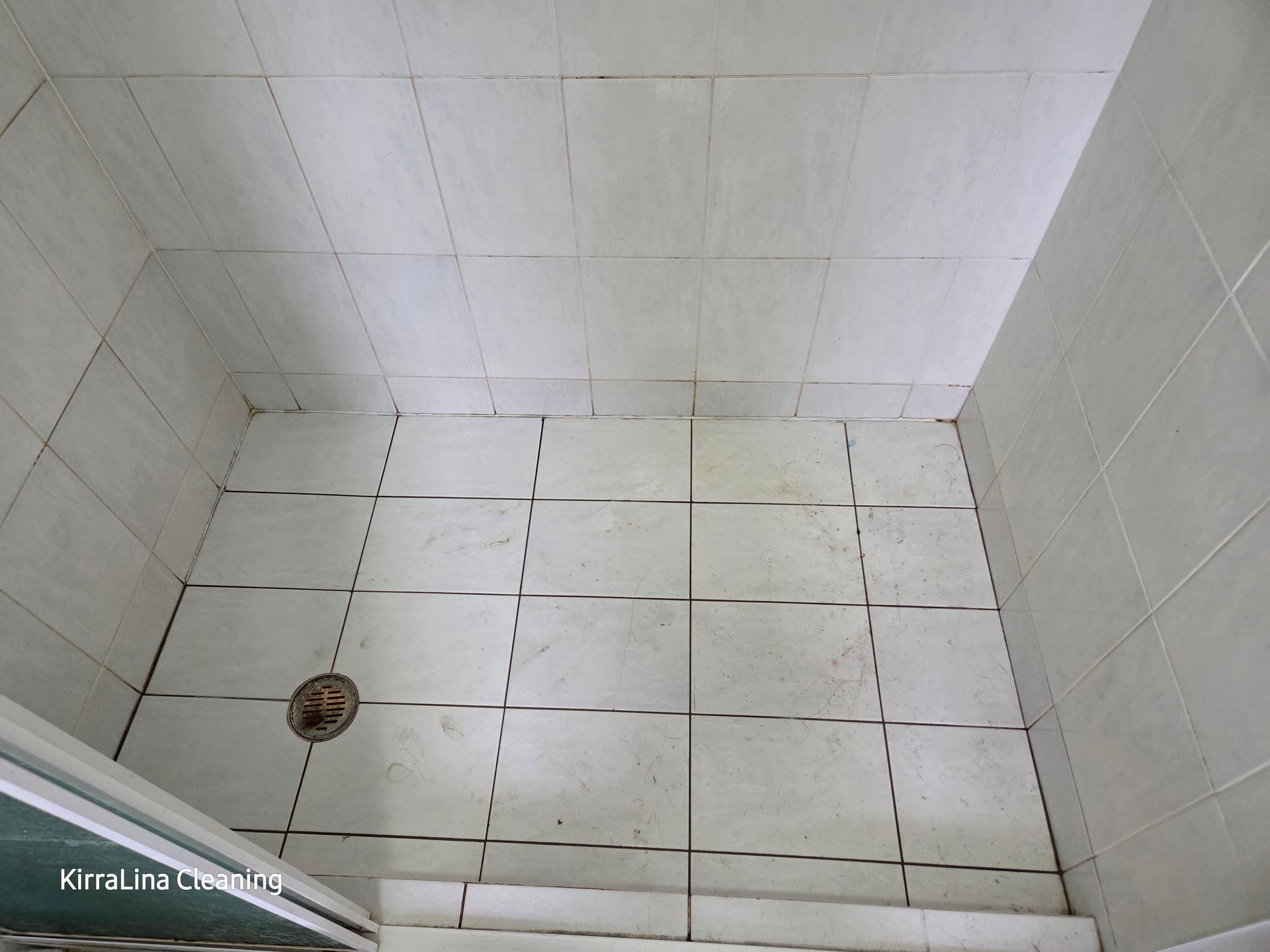 White tiled shower corner with a floor drain and dark grout stains. — KirraLina Cleaning Services in Tweed Heads, NSW