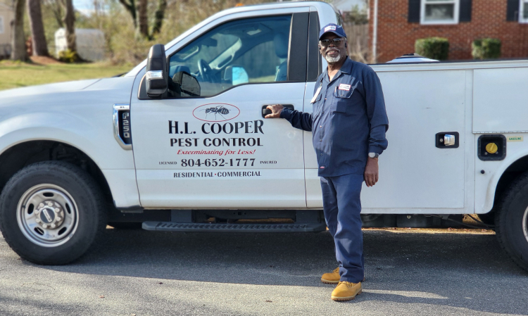 Man in blue uniform stands next to a white pest control truck. Company logo visible.