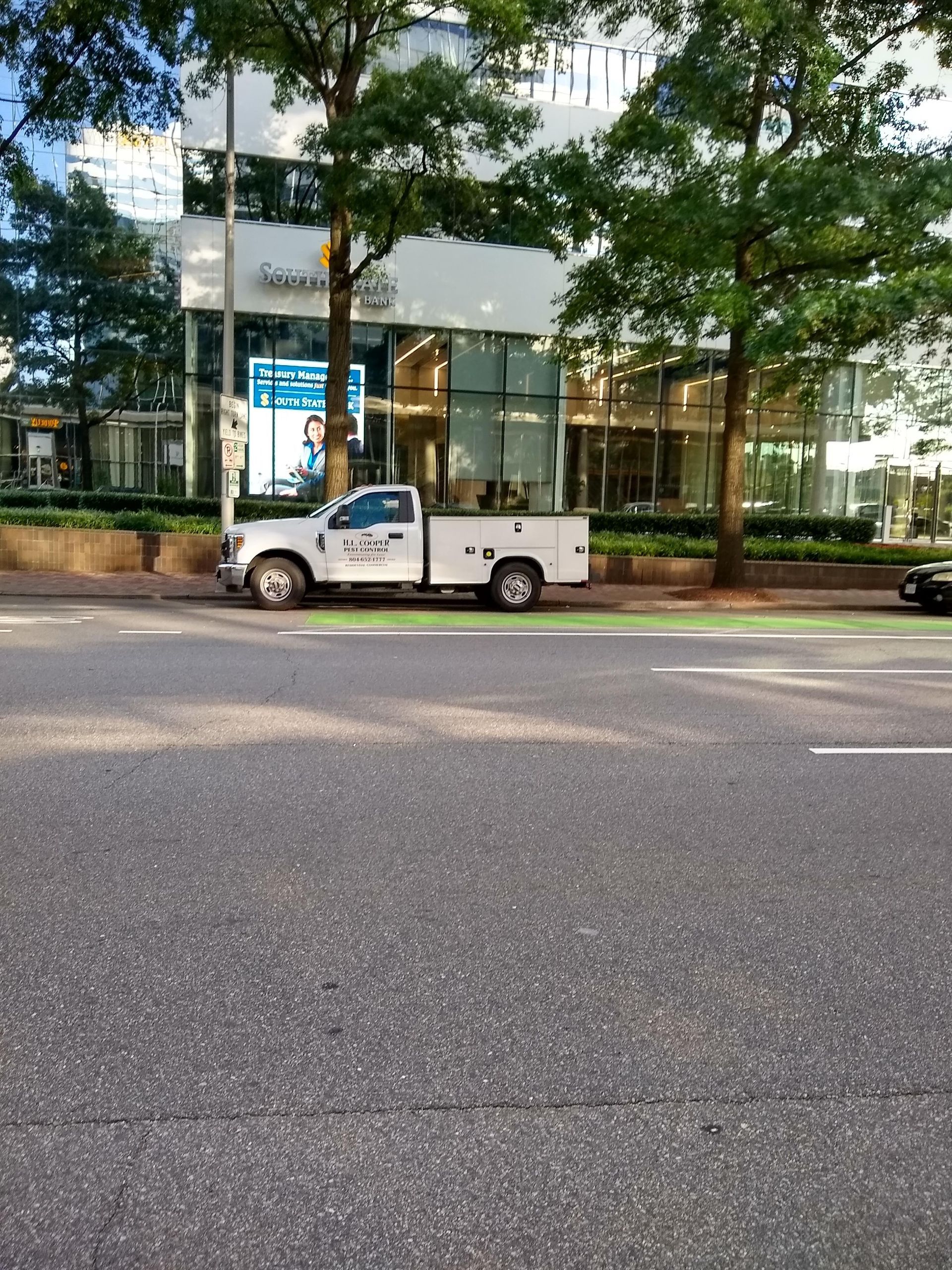 White truck parked by building and trees on a city street.