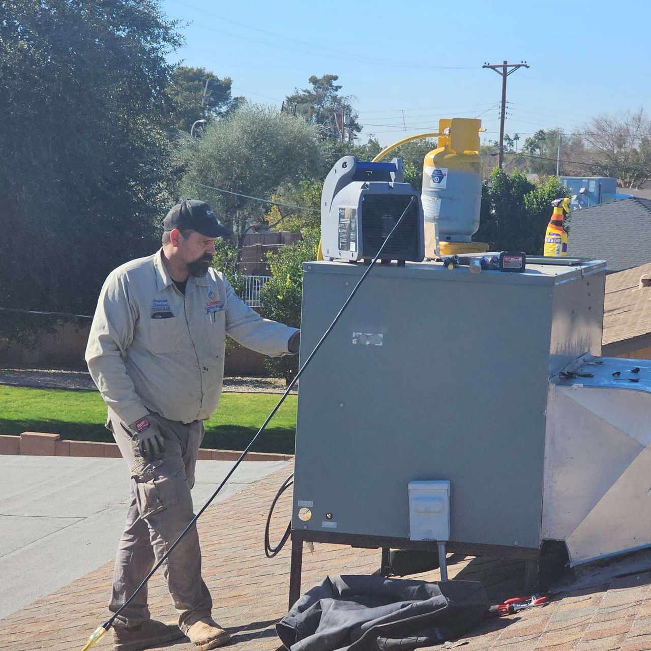 HVAC technician on a roof working on a unit. Gray unit, yellow tank, blue sky.
