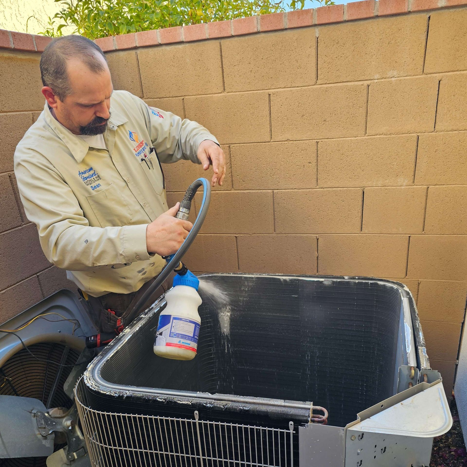 HVAC technician cleaning an air conditioning unit outside.