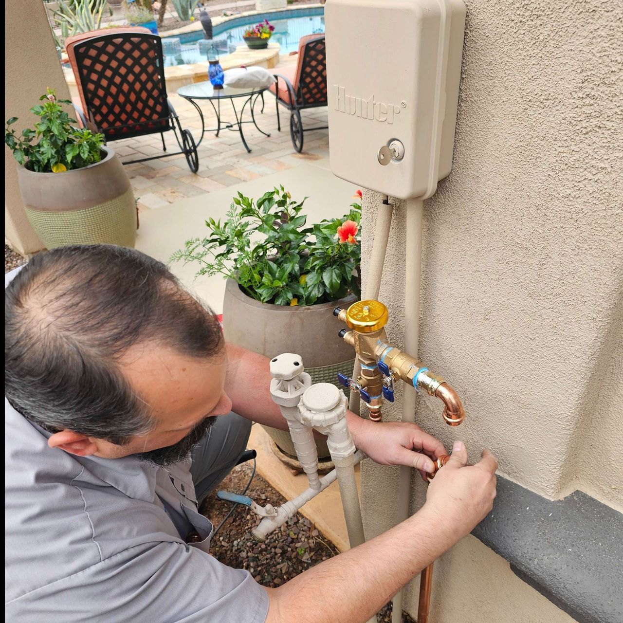 Man fixing a spigot on an exterior wall near a pool.