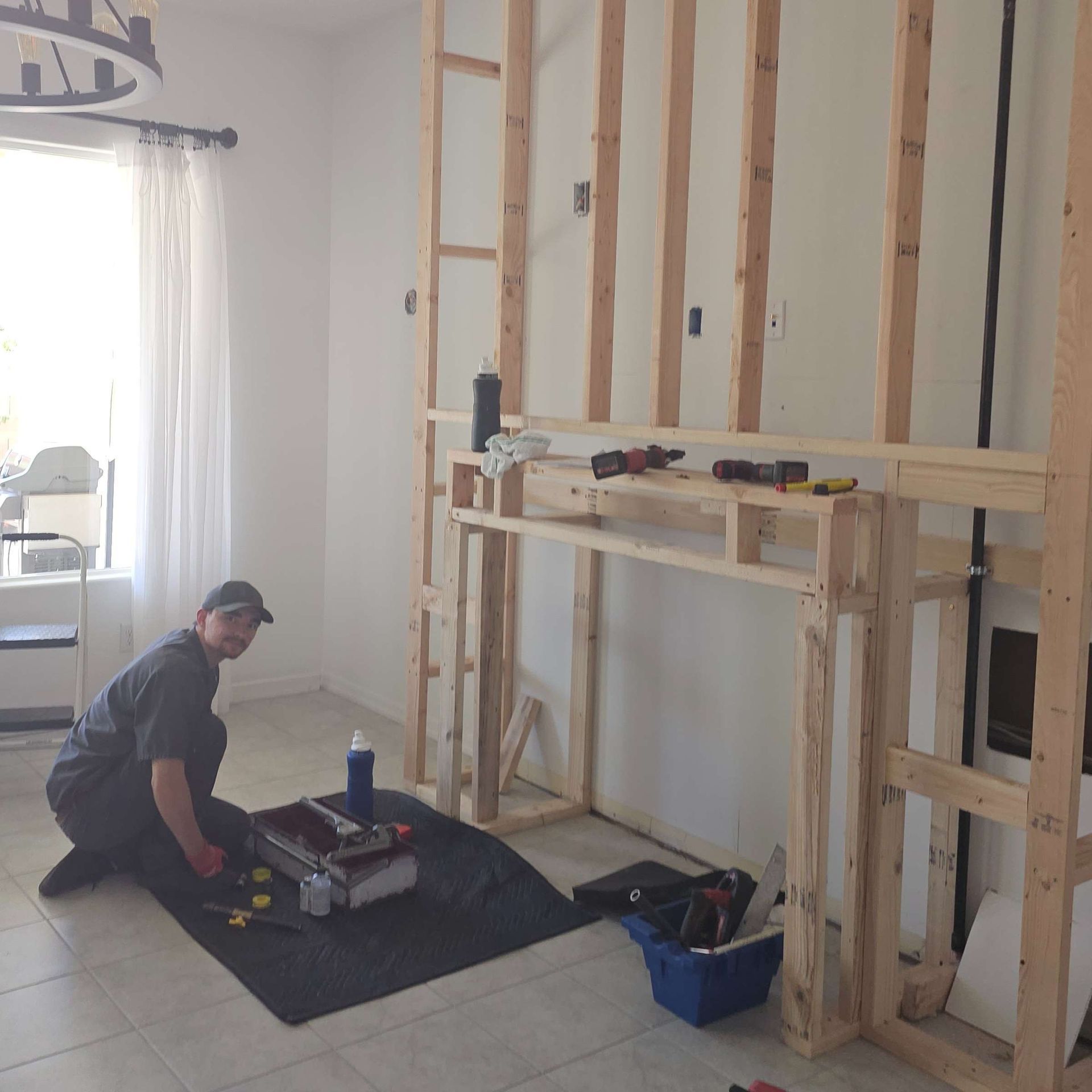 A person kneels near tools, framing a fireplace against a white wall, construction in progress.