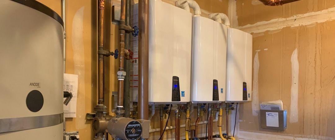 Three white boilers with copper pipes against a light brown wall, next to a water heater.