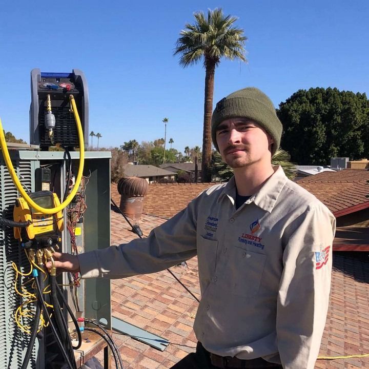 HVAC technician on a rooftop, pointing at machinery. He wears a green beanie and uniform under a sunny sky.
